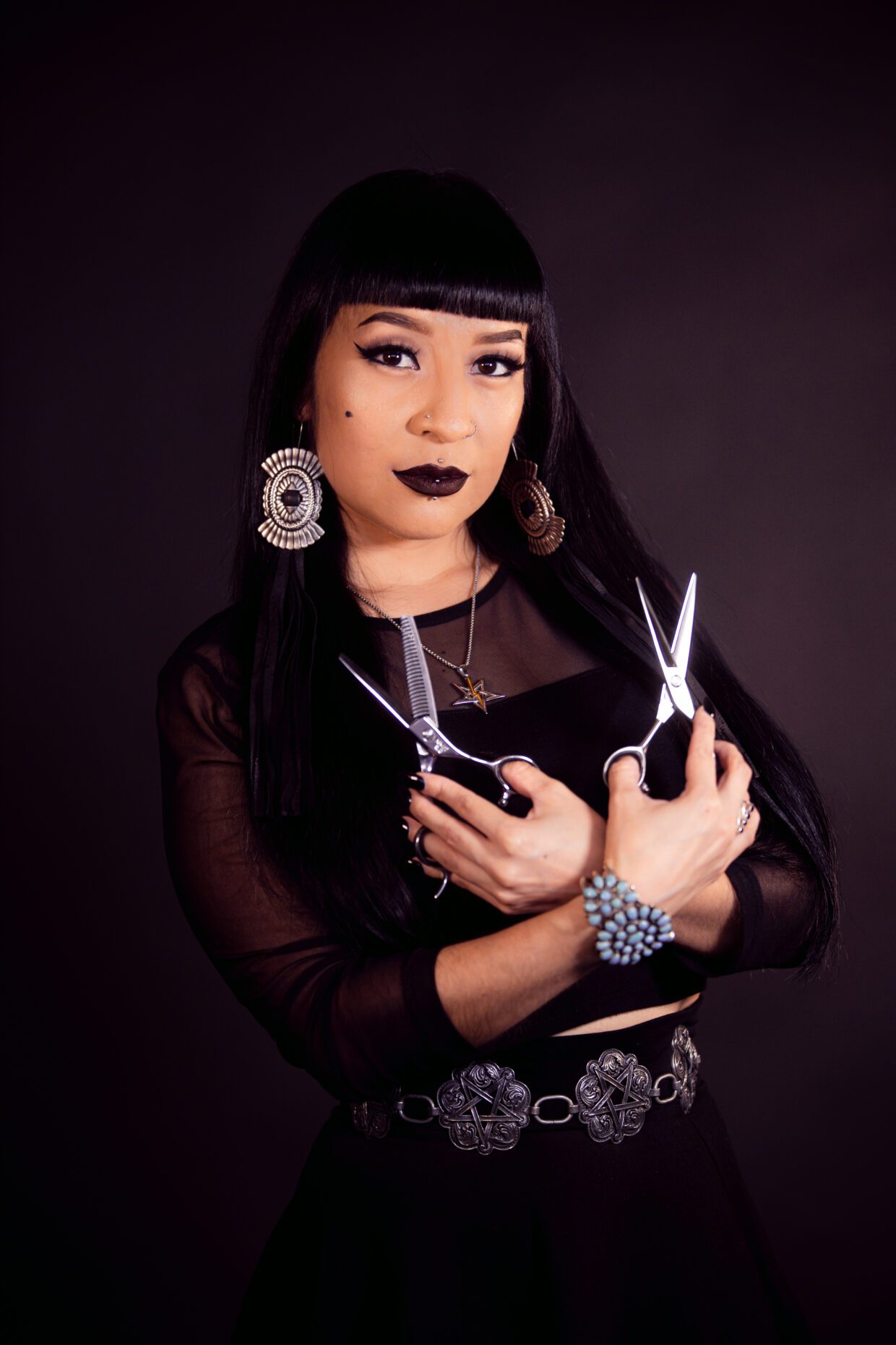 This shows Daphne Coriz, Indigenous hairstylist, posing with two pairs of hair cutting scissors.