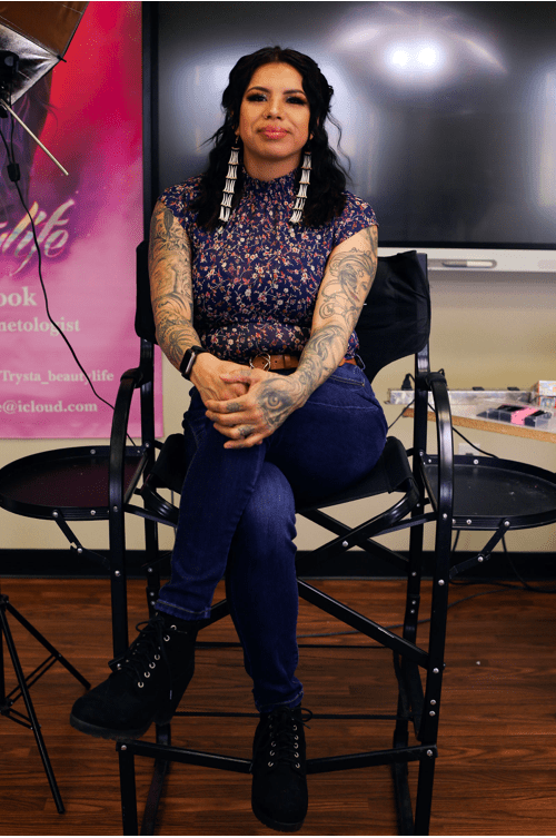 This shows Trysta Cook, Indigenous hairstyllist, posing while sitting in a chair at a photoshoot. 