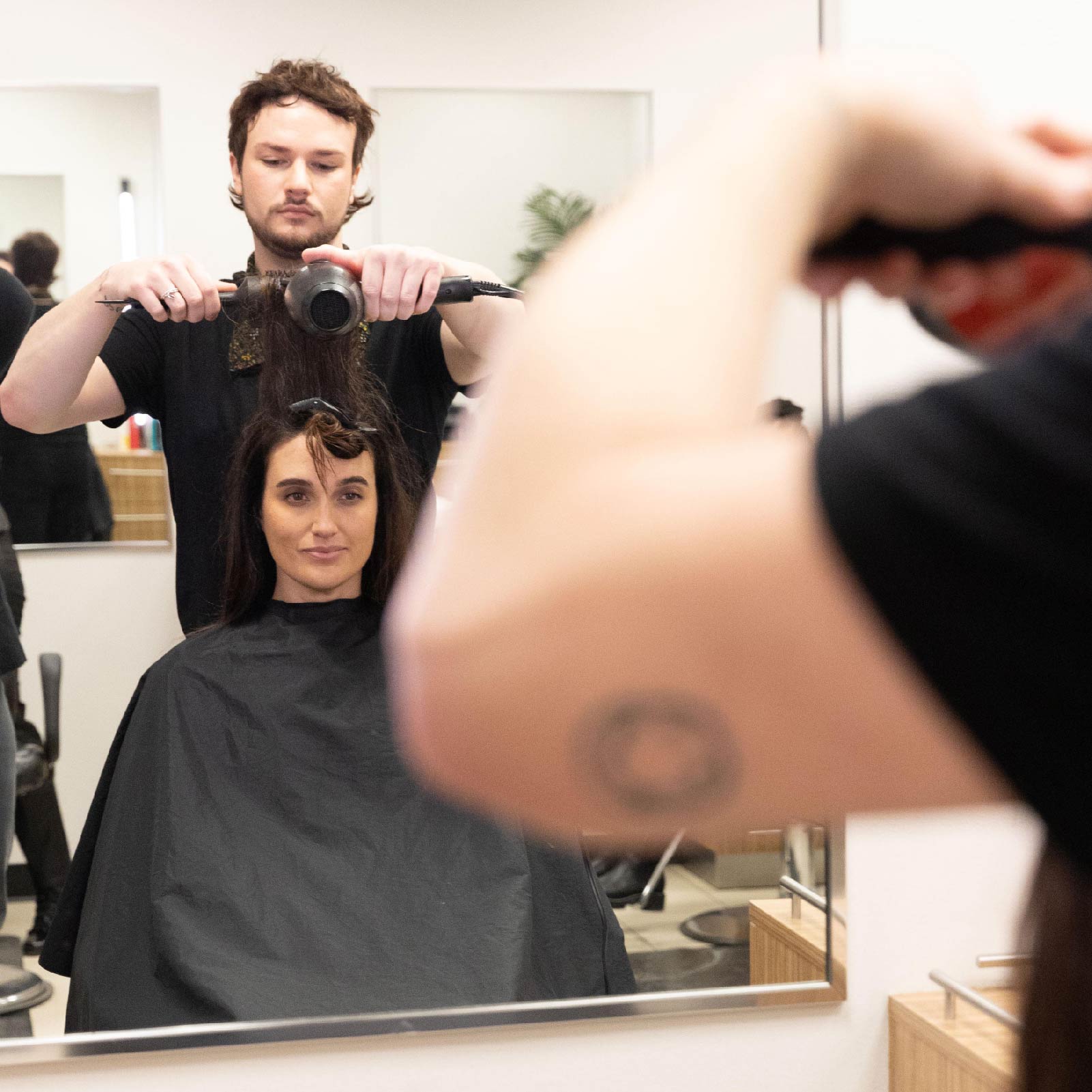 Hairdresser with a tattoo is giving a blow out to a client